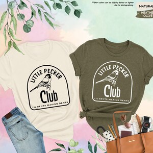 May include: Two t-shirts with a graphic of a bird in a circle with the text "Little Pecker Club" and "Lil Gents Making Dents". The shirt on the left is natural colored and the shirt on the right is heather olive.