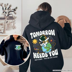 May include: Black hoodie with a graphic on the back showing an astronaut on Earth, the sun, and the text "TOMORROW NEEDS YOU." The front of the hoodie has a smaller graphic with the text "TOMORROW NEEDS YOU."