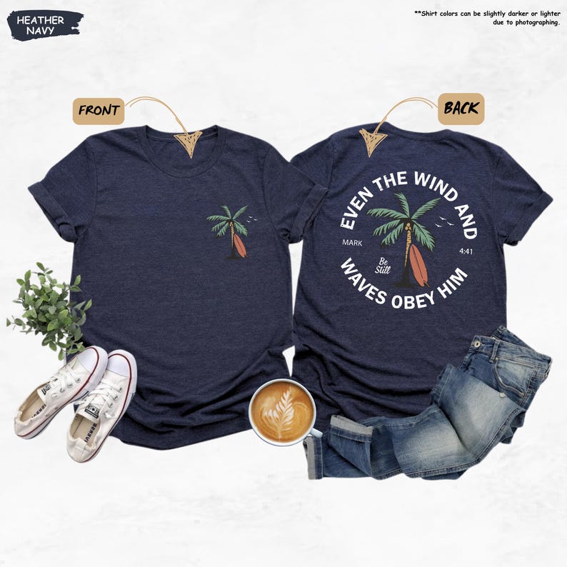 K&ouml;nnte beinhalten: Heather-Marineblaue T-Shirts mit einem Palmen- und Surfbrett-Motiv. Die Vorderseite des Shirts hat ein kleines Design, w&auml;hrend die R&uuml;ckseite ein gr&ouml;&szlig;eres kreisf&ouml;rmiges Design mit dem Text "Even the wind and waves obey him" aufweist.