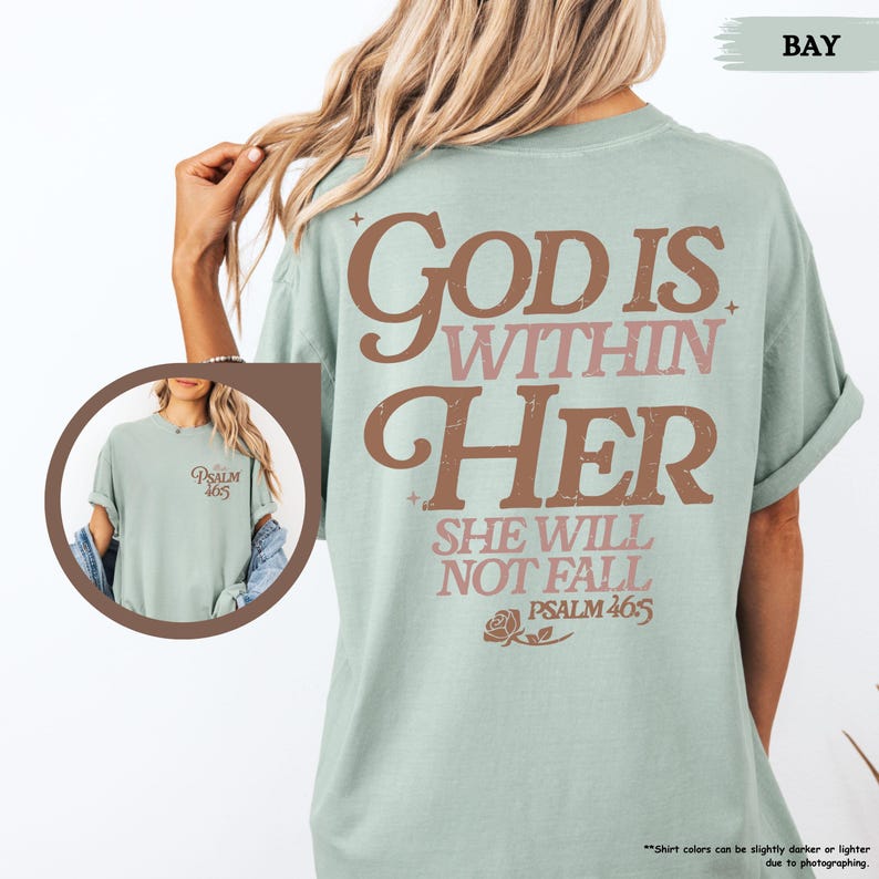 May include: A light green t-shirt with the text "God is Within Her, She Will Not Fall, Psalm 46:5" in brown and pink lettering. The shirt has a crew neck and short sleeves. The shirt is a relaxed fit.