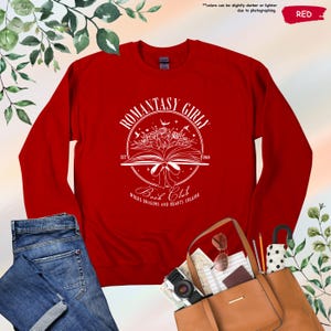 May include: Red long-sleeved shirt with a white graphic of an open book with flowers and the text "Romantasy Girly Book Club Where Dragons and Hearts Collide"
