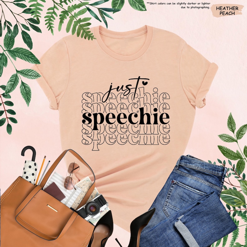 Puede incluir: Una camiseta de color melocot&oacute;n con el texto "just speechie" en letras negras repetidas en un patr&oacute;n apilado.
