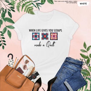 May include: White t-shirt with the text "WHEN LIFE GIVES YOU SCRAPS make a Quilt" and three colorful quilt block designs. The shirt is paired with blue jeans, a brown tote bag, and other accessories.