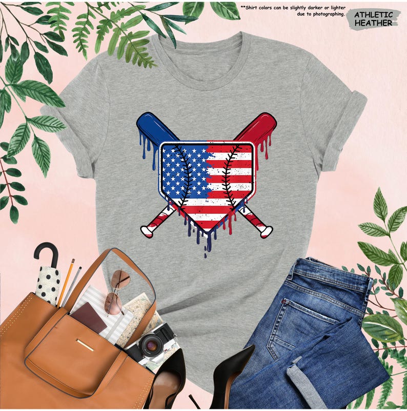 K&ouml;nnte beinhalten: Graues Athletic Heather T-Shirt mit Baseball-Motiv. Das Motiv zeigt ein Schild mit dem Design der amerikanischen Flagge, gekreuzte Baseballschl&auml;ger und tropfende Farbeffekte in Rot, Wei&szlig; und Blau. Das T-Shirt wird mit einer blauen Jeans gezeigt.