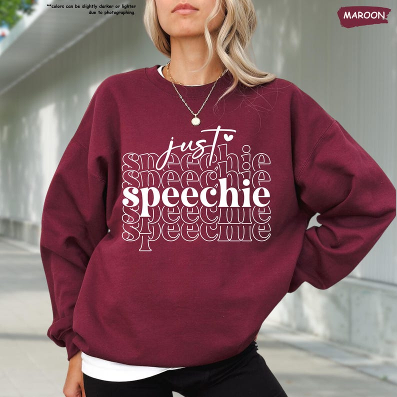 Puede incluir: Una sudadera color granate con el texto "just speechie" impreso en blanco. El texto se repite en un patr&oacute;n apilado con la palabra "speechie" en un tama&ntilde;o de fuente m&aacute;s grande.