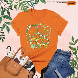 K&ouml;nnte beinhalten: Orangefarbenes T-Shirt mit einem Motiv aus drei Halsketten mit Kleebl&auml;ttern, einem Hufeisen und den Worten "One Lucky Teacher".