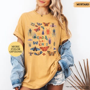 May include: Mustard-coloured t-shirt with a colourful insect and butterfly graphic and the text "BE KIND TO ALL KINDS." The shirt has short sleeves and a relaxed fit. More colour options are available.