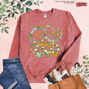 K&ouml;nnte beinhalten: Ein Sweatshirt in Heather-Scharlachrot mit einem Motiv aus drei Halsketten mit Kleebl&auml;ttern, einem Hufeisen und den Worten "One Lucky Teacher".