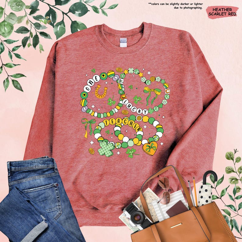 K&ouml;nnte beinhalten: Ein Sweatshirt in Heather-Scharlachrot mit einem Motiv aus drei Halsketten mit Kleebl&auml;ttern, einem Hufeisen und den Worten "One Lucky Teacher".
