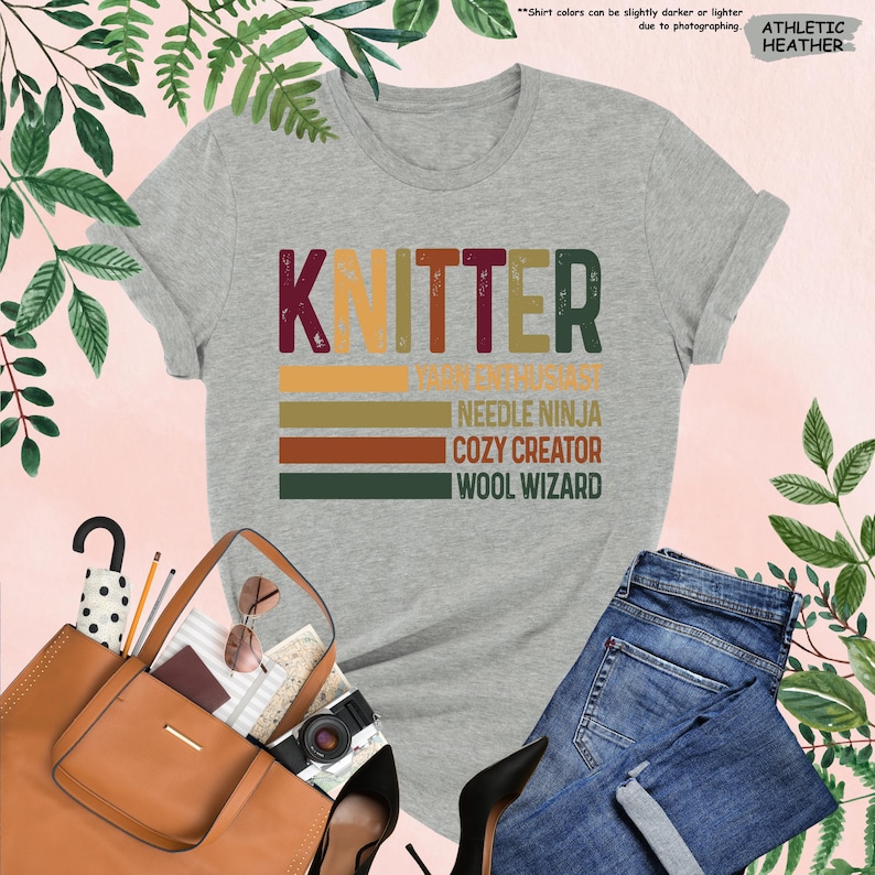 May include: A gray t-shirt with the word "Knitter" in a vintage style font. The text is layered with colorful stripes and the words "Yarn Enthusiast", "Needle Ninja", "Cozy Creator", and "Wool Wizard" are written below.