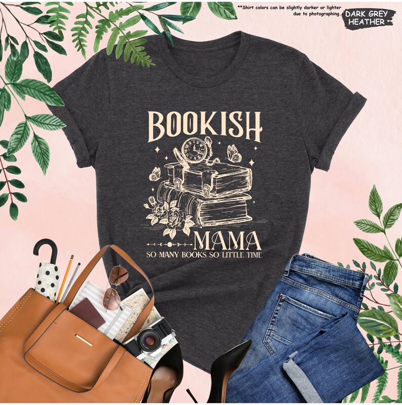 May include: Dark grey heather t-shirt with the words "BOOKISH MAMA" and "SO MANY BOOKS SO LITTLE TIME" printed on the front. The design features a stack of books, a clock, butterflies, and flowers. A brown tote bag and blue jeans are also visible.