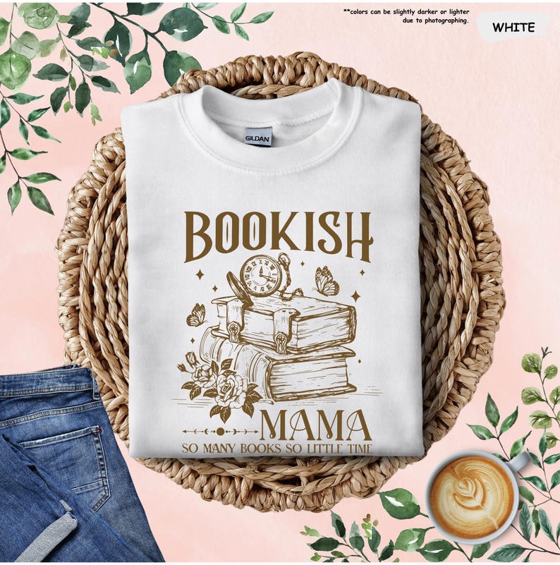May include: White sweatshirt with the text "BOOKISH MAMA" and a graphic of books, a clock, and butterflies. The phrase "SO MANY BOOKS SO LITTLE TIME" is below the graphic. The sweatshirt is on a woven basket.