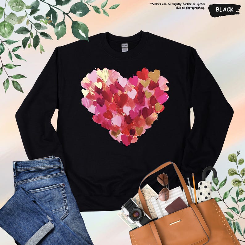 Pu&ograve; includere: Felpa nera con un grande cuore composto da pennellate stratificate nei toni del rosso, rosa e oro. Il testo "colors can be slightly darker or lighter due to photographing" &egrave; visibile. Anche la parola "BLACK" &egrave; visibile.