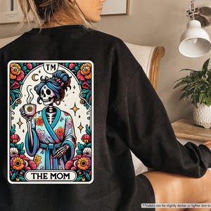 May include: Black sweatshirt with a colorful graphic of a skeleton wearing a robe and holding a cup of coffee. The graphic is in the style of a tarot card and says "The Mom" at the bottom.