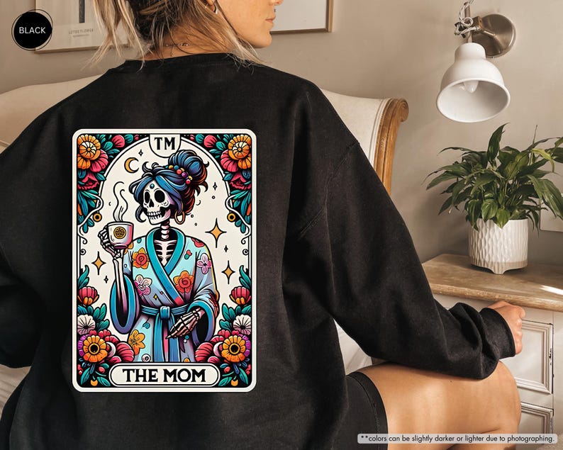 May include: Black sweatshirt with a colorful graphic of a skeleton wearing a robe and holding a cup of coffee. The graphic is in the style of a tarot card and says "The Mom" at the bottom.
