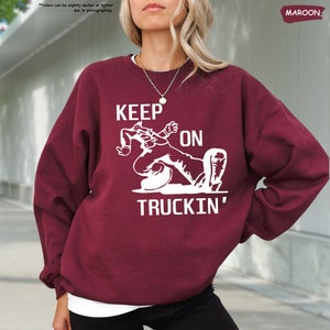 a woman with blonde hair wearing a maroon sweatshirt that says keep on truckin