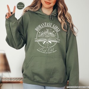 May include: A green hooded sweatshirt with a white graphic design that says "Romantasy Girl Book Club" with a book, flowers, and stars. The text below the graphic says "Where Dragons and Hearts Collide."