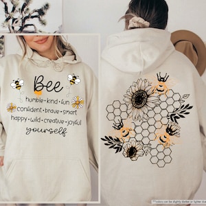 May include: A beige hoodie with a bee design and the text "Bee humble. kind. fun. confident. brave. smart. happy. wild. creative. joyful yourself".
