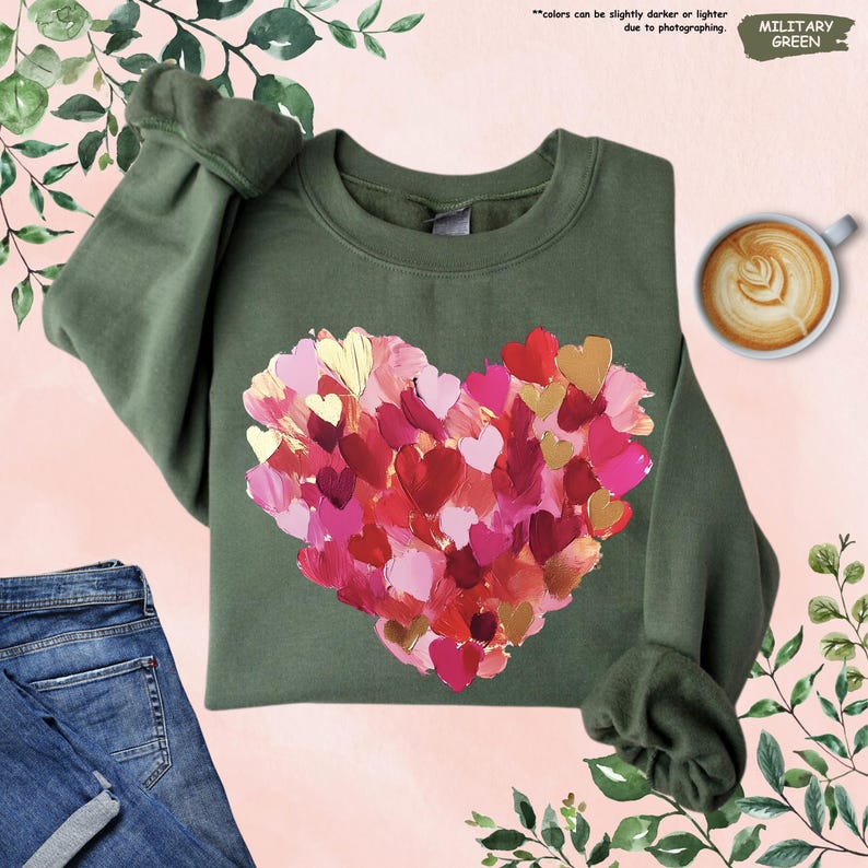 Pu&ograve; includere: Felpa verde militare con un design a cuore composto da cuori a pennellate in rosso, rosa e oro. La felpa ha un girocollo e maniche lunghe. Il testo "colors can be slightly darker or lighter due to photographing" &egrave; visibile.