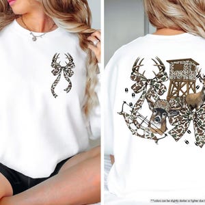 May include: White sweatshirt with a deer antler bow design on the front and back. The back features a deer, hunting blind, bow and arrow, and deer tracks, all in a camouflage pattern.