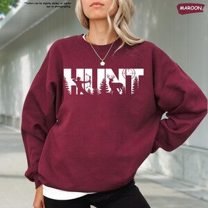 a woman with blonde hair wearing a maroon sweatshirt and black pants