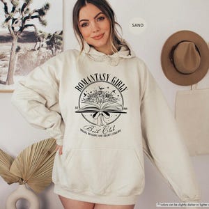 May include: A cream-coloured hoodie with a black graphic of a book with flowers and the text "Romantasy Girl Book Club Where Dragons and Hearts Collide".