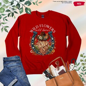 May include: Red long-sleeve shirt with a graphic of a woman with long blonde hair wearing a cowboy hat and a horseshoe with the text "WILD FLOWERS wild horses".