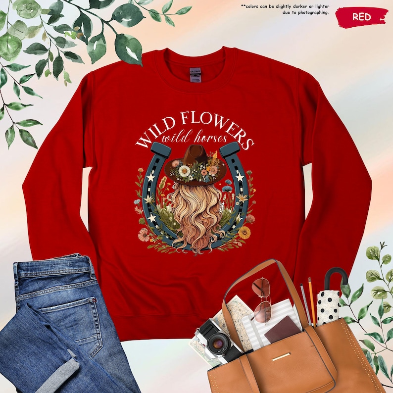 May include: Red long-sleeve shirt with a graphic of a woman with long blonde hair wearing a cowboy hat and a horseshoe with the text "WILD FLOWERS wild horses".