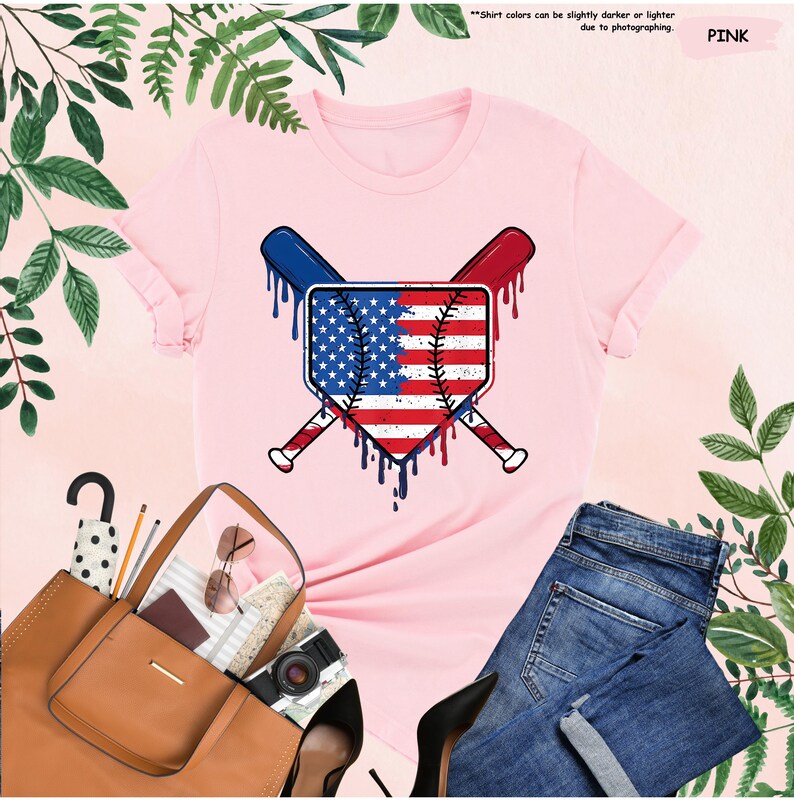 K&ouml;nnte beinhalten: Hellrosa T-Shirt mit einem Baseball-Motiv im Design der amerikanischen Flagge. Das Design umfasst gekreuzte Schl&auml;ger und tropfende Farbeffekte. Das Shirt wird mit blauen Jeans, einer braunen Tragetasche und schwarzen Abs&auml;tzen pr&auml;sentiert.