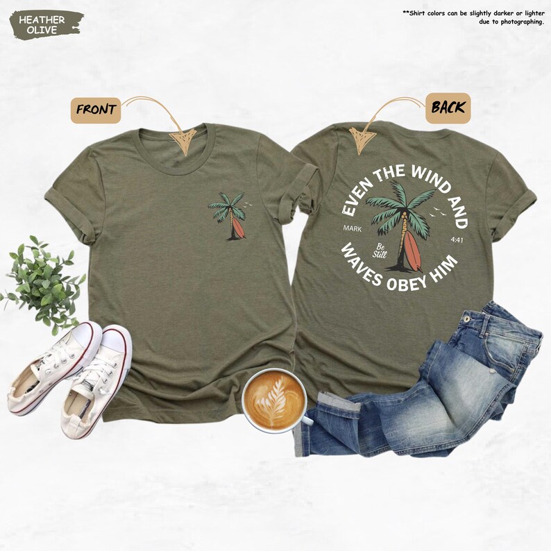 K&ouml;nnte beinhalten: Heather-olivfarbene T-Shirts mit einem Palmen- und Surfbrett-Motiv. Die Vorderseite des T-Shirts hat ein kleines Palmen-Design. Die R&uuml;ckseite des T-Shirts hat ein gr&ouml;&szlig;eres Design mit dem Text "Even the wind and waves obey him".