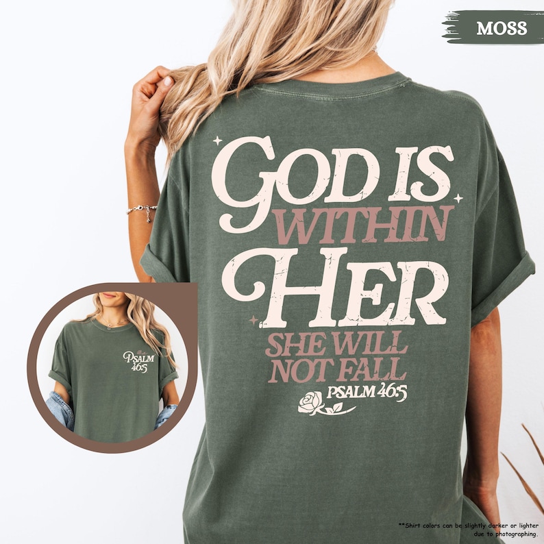 May include: Moss green t-shirt with the text "God is Within Her, She Will Not Fall, Psalm 46:5" in white and mauve lettering. The back of the shirt features the main text, while the front has a smaller design. The shirt is a comfortable, casual style.