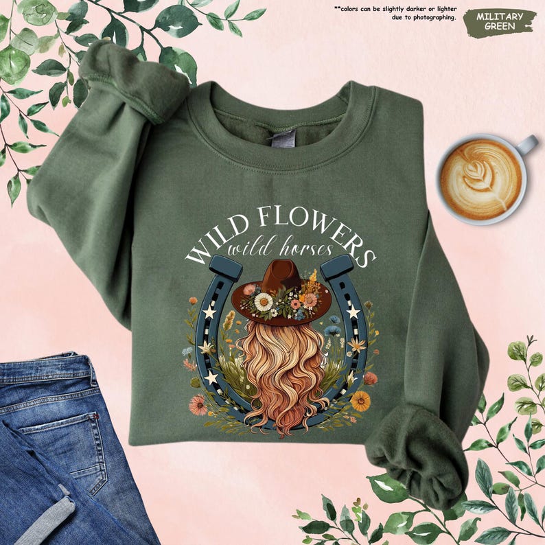 May include: A green sweatshirt with a graphic print of a woman with long blonde hair wearing a floral hat and a horseshoe with stars. The text "WILD FLOWERS wild horses" is printed above the graphic.
