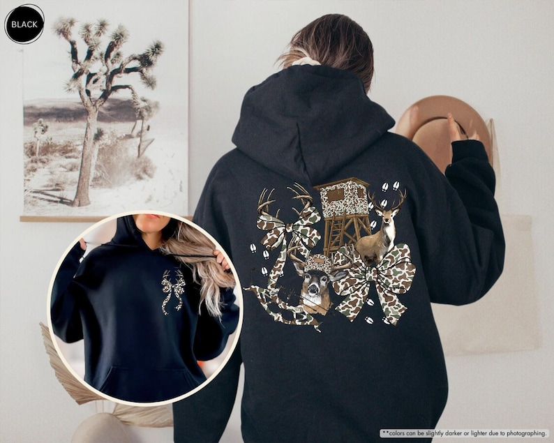 May include: Black hooded sweatshirt with a hunting-themed graphic on the back. The design features a deer, a hunting blind, and camouflage bows. The sweatshirt has a front pocket and a drawstring hood.