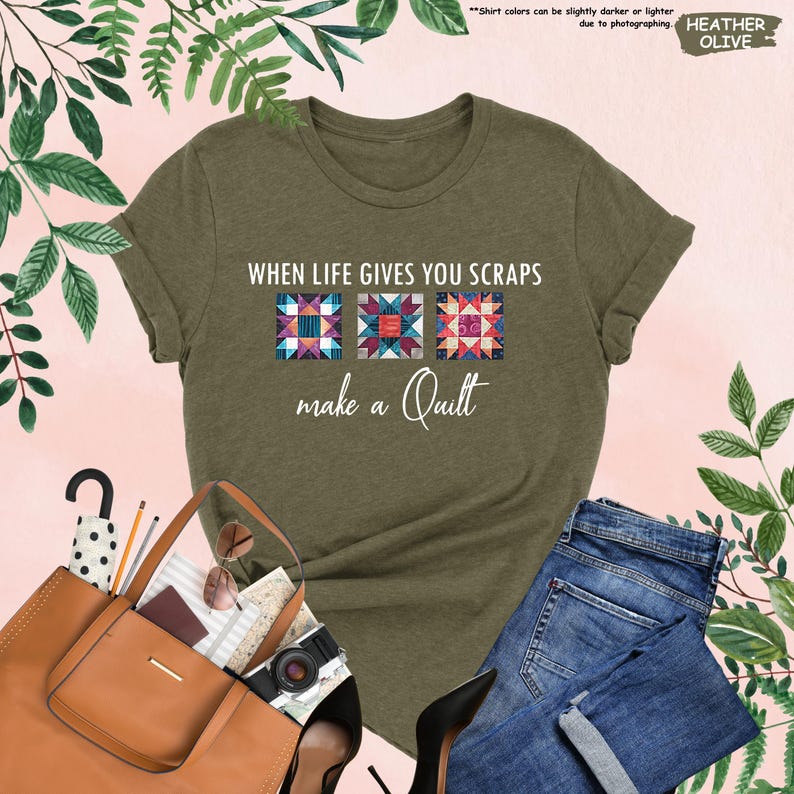 May include: Olive green t-shirt with the text "WHEN LIFE GIVES YOU SCRAPS make a Quilt" and three quilt block designs. The shirt is paired with blue jeans, a brown purse, and black heels. The shirt's color is Heather Olive.