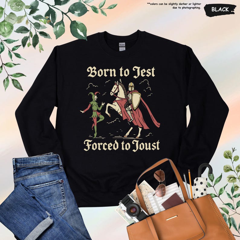 K&ouml;nnte beinhalten: Schwarzes Sweatshirt mit dem Text "Born to Jest Forced to Joust" in einer mittelalterlichen Schriftart. Die Grafik zeigt einen Narren und einen Ritter zu Pferd. Das Sweatshirt ist schwarz.