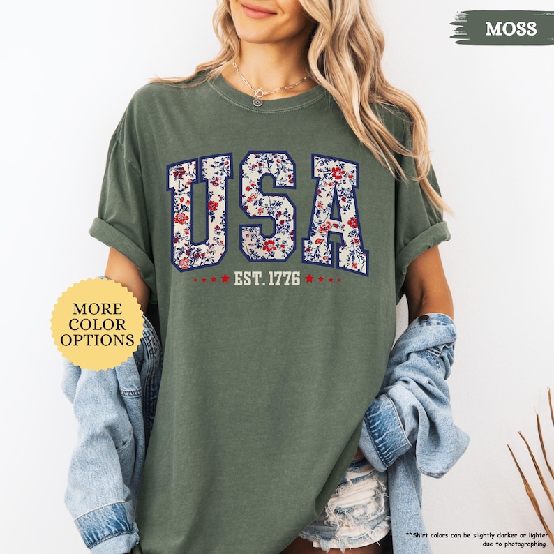 May include: A green t-shirt with a floral print of the word "USA" and the text "EST. 1776".