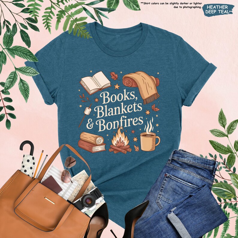 May include: A teal t-shirt with the text "Books, Blankets & Bonfires" and illustrations of a book, blanket, campfire, and mug. The shirt is paired with blue jeans, a brown tote bag, and black heels.