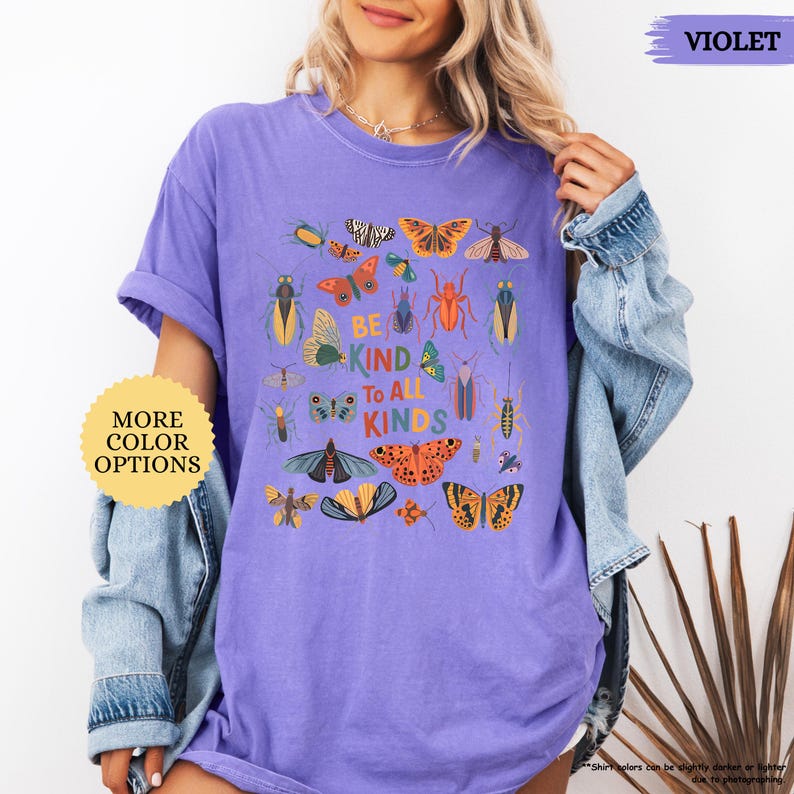 May include: A lilac t-shirt with a design of various insects and butterflies. The text "BE KIND TO ALL KINDS" is printed on the front. A button on the left says "MORE COLOR OPTIONS".