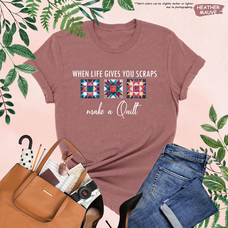 May include: Heather mauve t-shirt with the text "WHEN LIFE GIVES YOU SCRAPS make a Quilt." The shirt features three colorful quilt block designs. The shirt is paired with blue jeans, a brown purse, and black heels. The words "HEATHER MAUVE" are also visible.