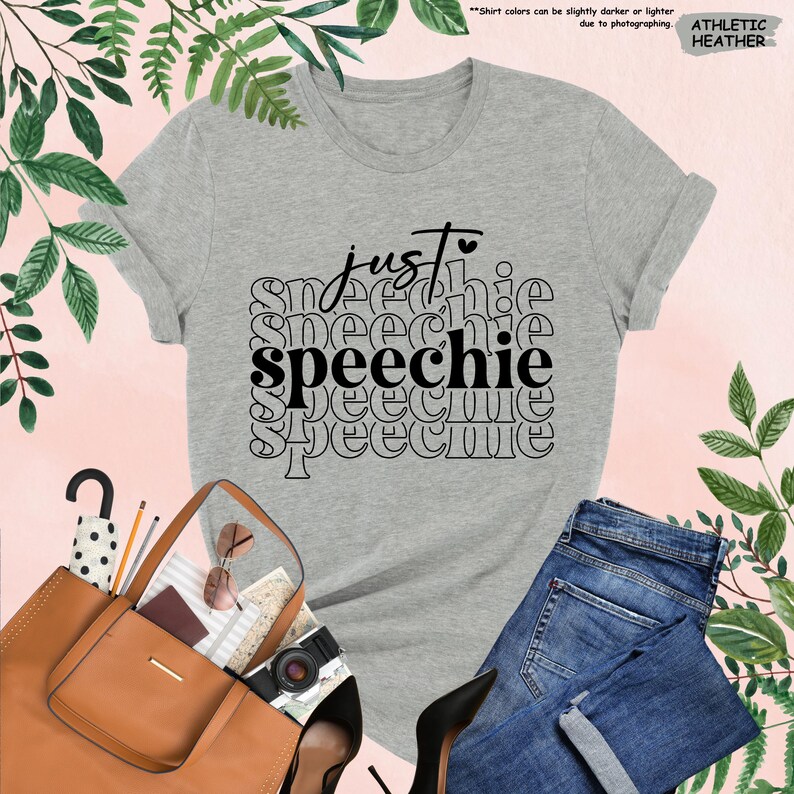 Puede incluir: Una camiseta gris jaspeada con el texto "just speechie" impreso en negro. El texto se repite varias veces en un patr&oacute;n apilado.