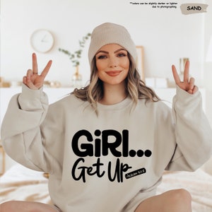 a woman sitting on a bed wearing a sweatshirt that says girl get up