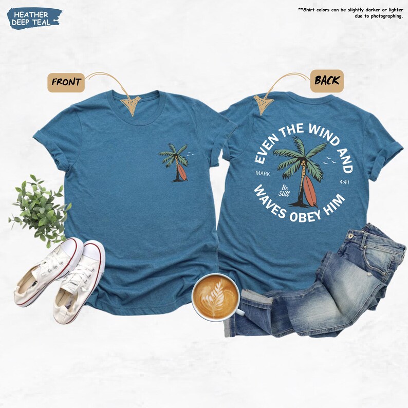 K&ouml;nnte beinhalten: T-Shirts in tiefem Teal mit einem Palmen- und Surfbrett-Motiv. Die Vorderseite des Shirts hat ein kleines Design, w&auml;hrend die R&uuml;ckseite ein gr&ouml;&szlig;eres Design mit dem Text "Even the wind and waves obey him" aufweist.