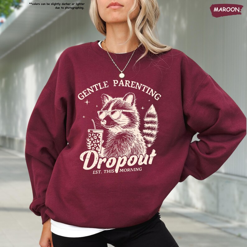 May include: Maroon sweatshirt with the text "GENTLE PARENTING Dropout EST. THIS MORNING" and a raccoon wearing sunglasses and holding a drink. The sweatshirt is a solid maroon color.