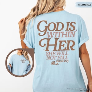 May include: Light blue t-shirt with the text "GOD IS WITHIN HER" in brown and pink lettering. The shirt also features the text "SHE WILL NOT FALL" and "PSALM 46:5". A small image of the shirt is in the lower left corner.