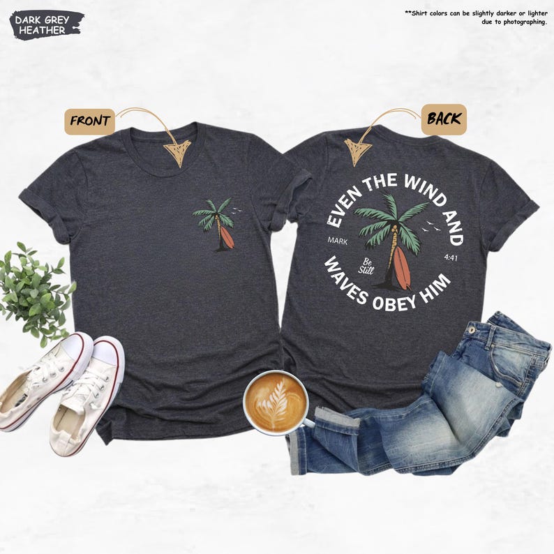 K&ouml;nnte beinhalten: Dunkelgraue melierte T-Shirts mit Designs auf der Vorder- und R&uuml;ckseite. Die Vorderseite zeigt eine Palme und ein Surfbrett. Auf der R&uuml;ckseite steht der Text "EVEN THE WIND AND WAVES OBEY HIM". Enth&auml;lt ein Paar wei&szlig;e Turnschuhe und eine Tasse Kaffee.