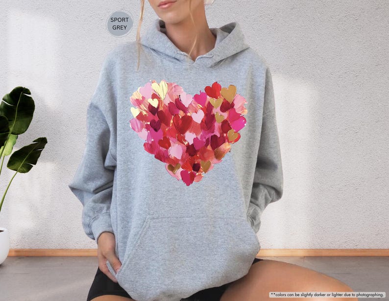 Pu&ograve; includere: Felpa con cappuccio grigio sportivo con un grande design a cuore realizzato con pennellate rosse, rosa e oro. La felpa con cappuccio ha un cappuccio con coulisse e una tasca frontale. Il testo "SPORT GREY" &egrave; in un cerchio in alto.