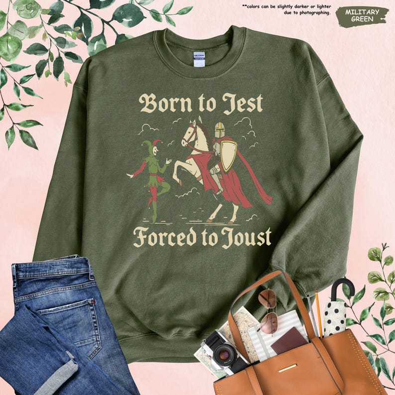 K&ouml;nnte beinhalten: Milit&auml;rgr&uuml;nes Sweatshirt mit dem Text "Born to Jest Forced to Joust" und einer Grafik eines Narren und eines Ritters zu Pferd. Das Sweatshirt ist ein Rundhals-Modell.