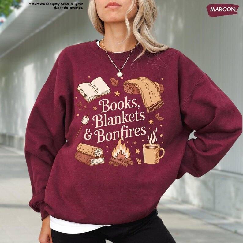 May include: Maroon sweatshirt with the text "Books, Blankets & Bonfires" and illustrations of a book, blanket, bonfire, and coffee cup. The sweatshirt is a solid maroon color.