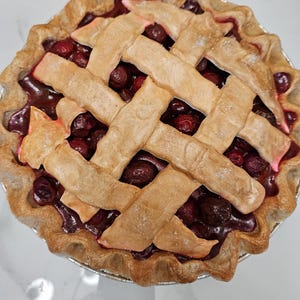 May include: A freshly baked cherry pie with a lattice crust. The pie features a golden-brown, crimped crust and a lattice top made of woven strips of dough. The filling is a deep red color, filled with cherries.