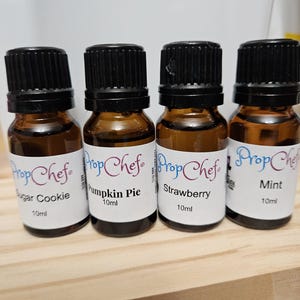 May include: Four small brown glass bottles with black lids and white labels. The labels read "Prop Chef" and list different flavors: Sugar Cookie, Pumpkin Pie, Strawberry, and Mint. Each bottle contains 10 ml of flavoring.